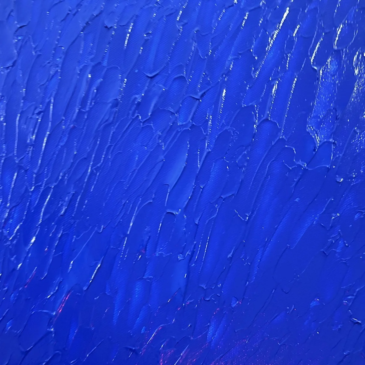 A close-up view of textured blue acrylic paint with rhythmic, heavy ridges on canvas and subtle hints of pink.