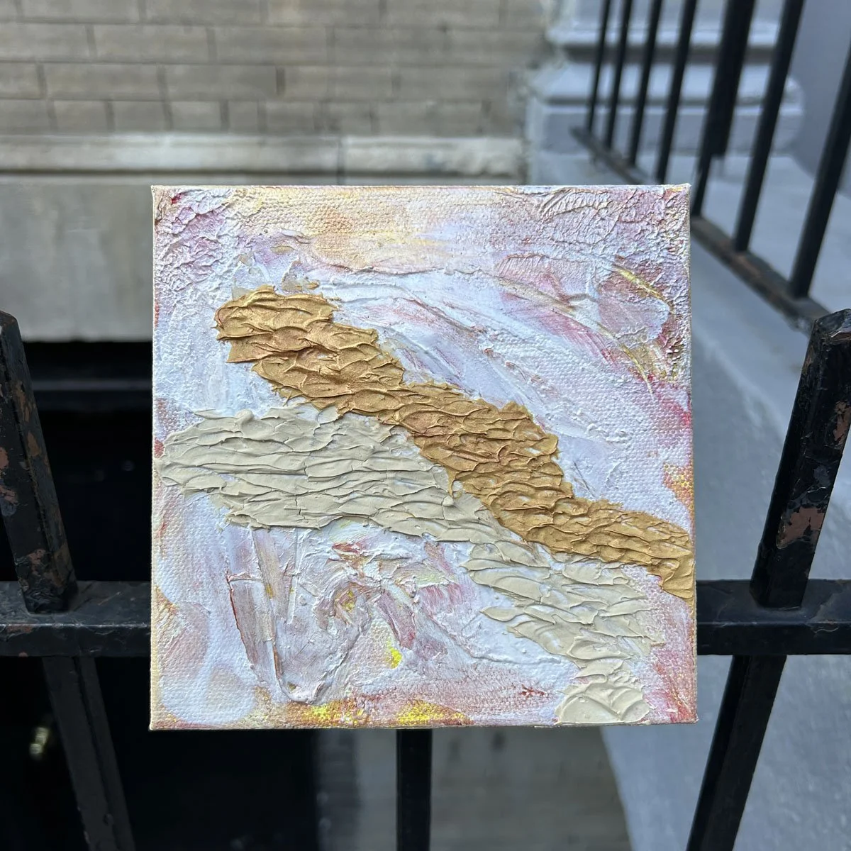 Small 6x6 textured abstract painting Road to Nowhere presented outdoors, held against a city iron railing, highlighting the 1.5" deep gallery profile.