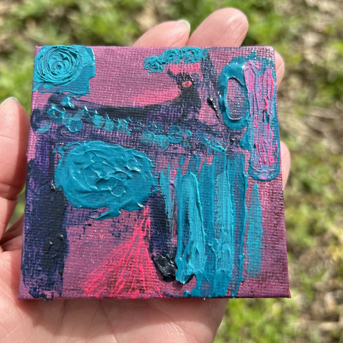 Close-up of a small square canvas with vibrant turquoise impasto textures on a purple and pink background.