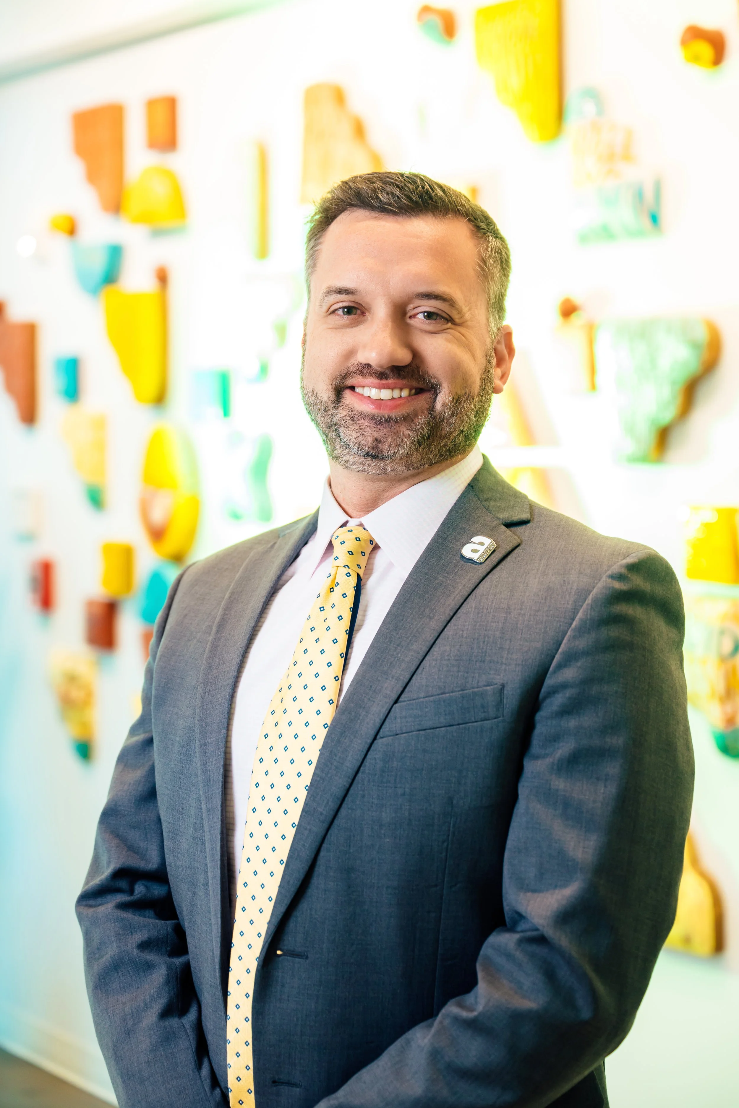 A smiling man in a business suit standing in front of a colorful wall display.