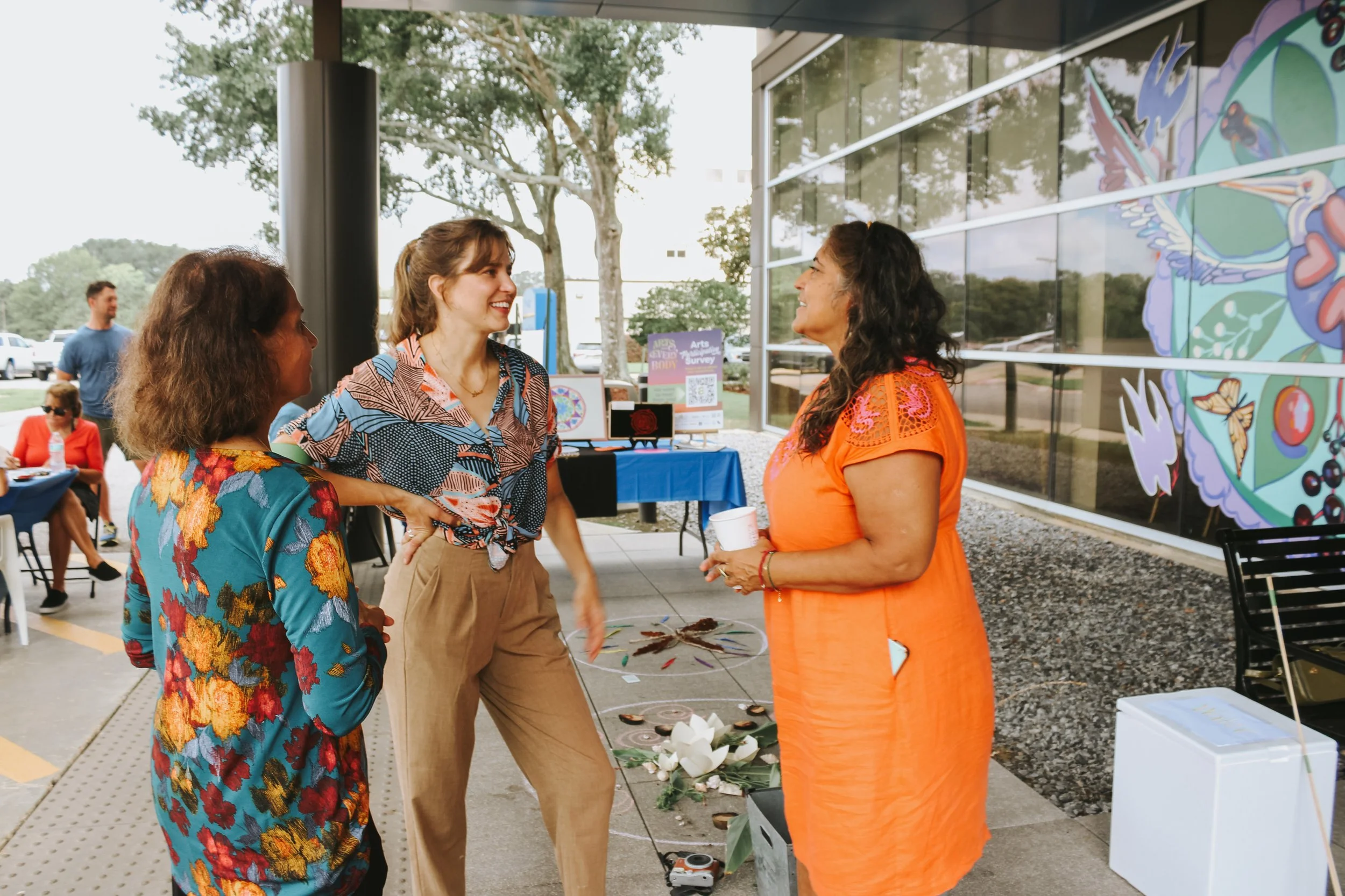 Three women are standing and talking outside a modern building about a mural they completed.