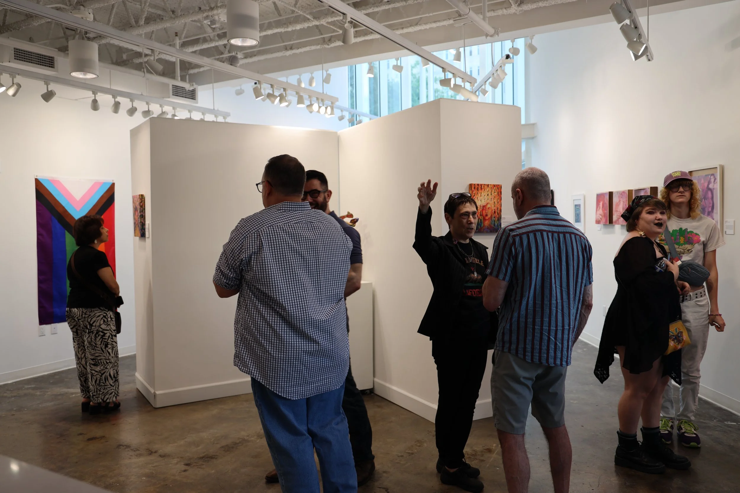 People gathered in an art gallery, engaging in conversation and viewing artwork displayed on white walls.