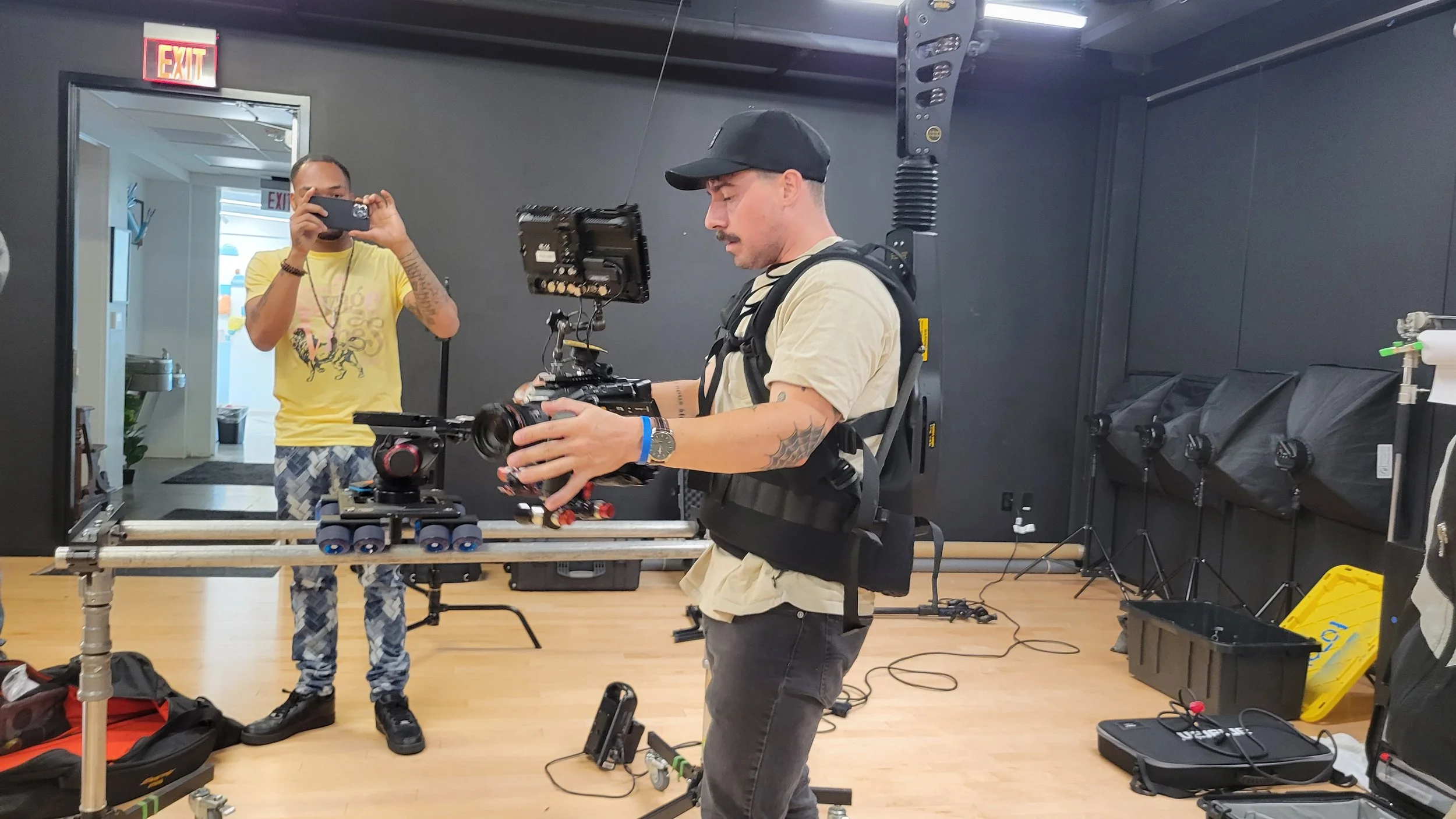 Two men working with camera and filming equipment in a studio setting, one of them is recording while the other holds a camera.