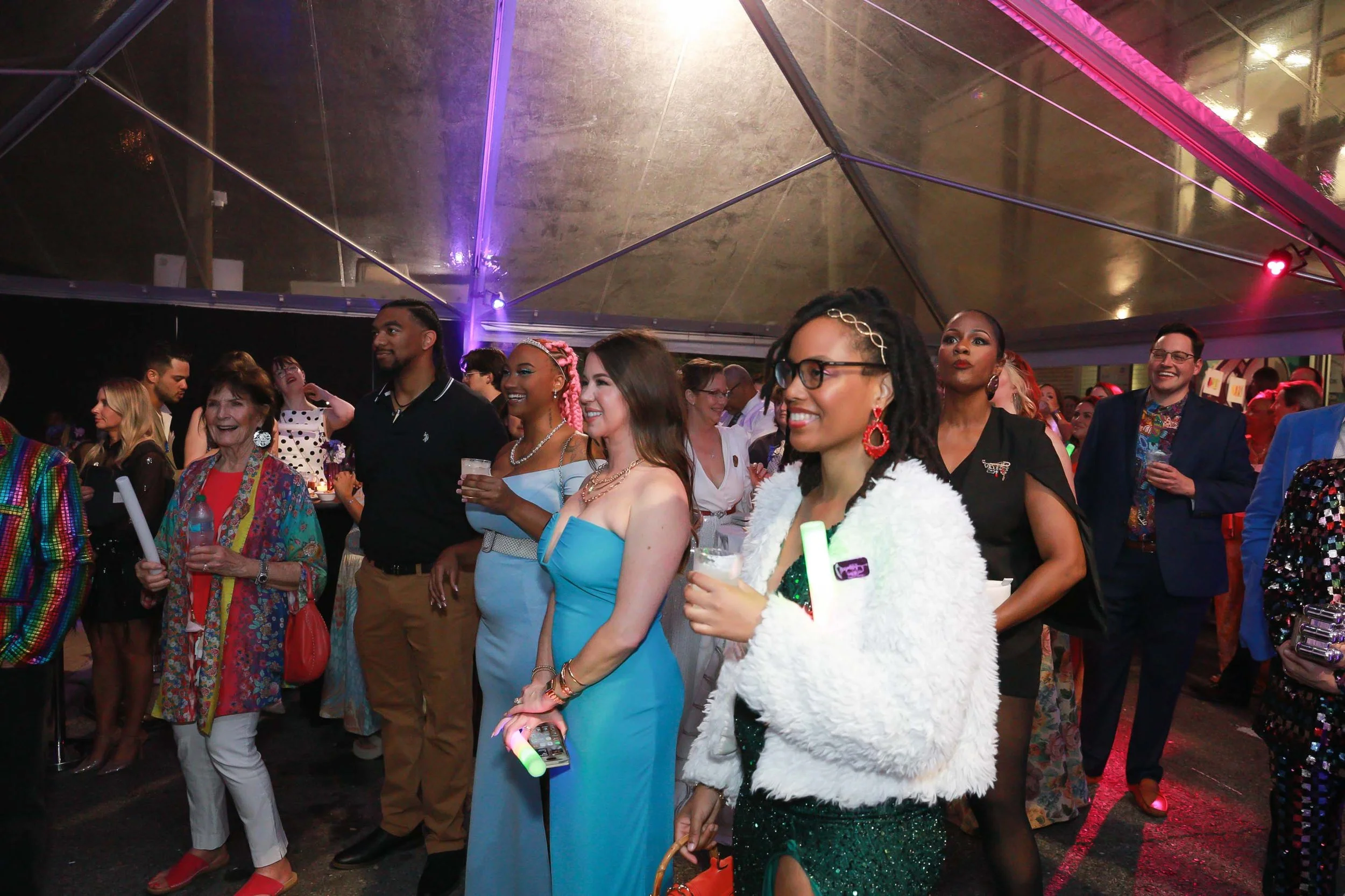 Group of diverse people dancing and enjoying at a vibrant indoor party with colorful lighting and reflective metallic ceiling.