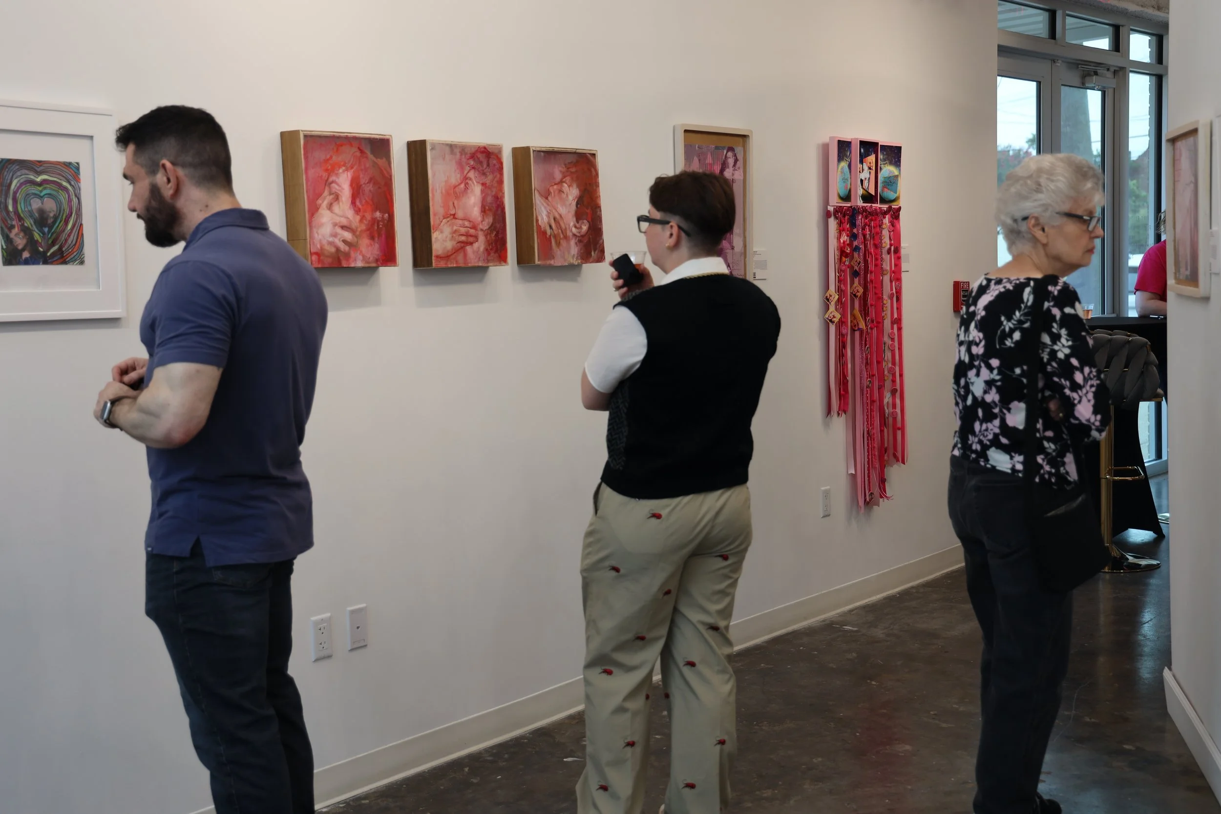 People viewing artwork at an art gallery with paintings and hanging decorations on the wall.