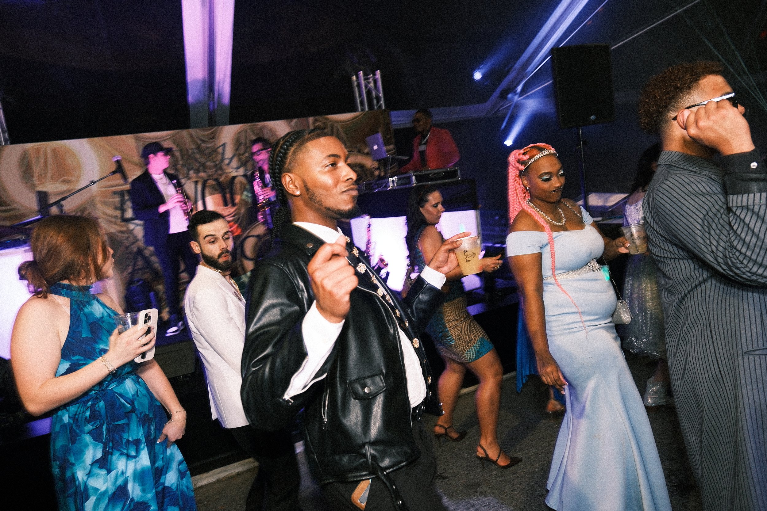 People at a lively social event or party, dancing and holding drinks under colorful lighting.