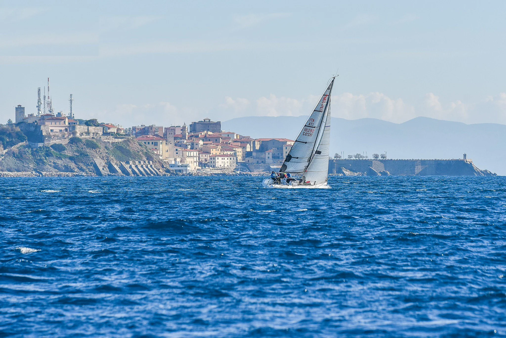 Vela con una città sullo sfondo, vista dal mare
