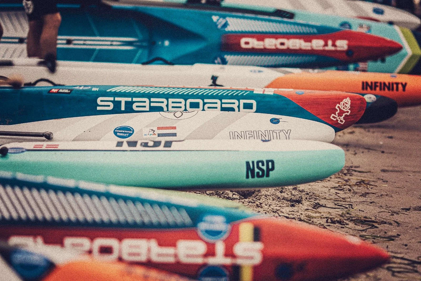 Sulle spiagge di sabbia, diverse tavole da surf colorate sono allineate, con il mare come sfondo.