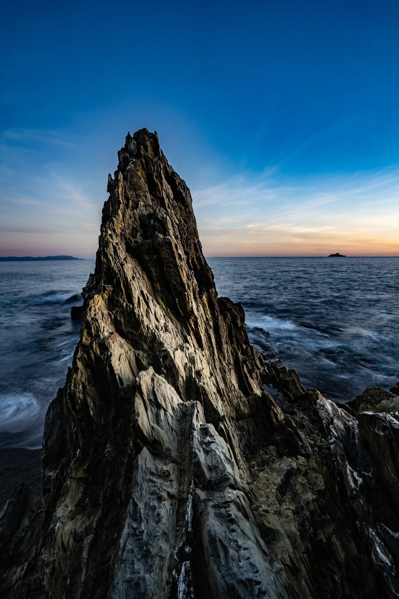 Una grande roccia appuntita nel mare con un cielo sereno al tramonto.