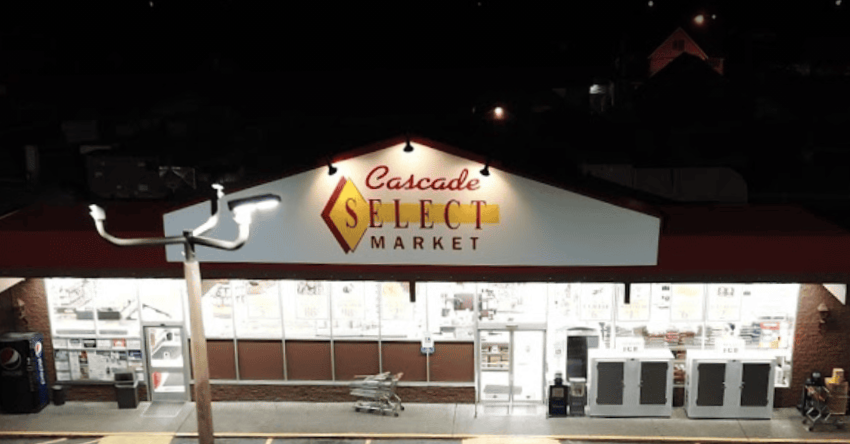 Nighttime view of Cascade Select Market storefront with illuminated sign, shopping carts outside, and entrance doors.
