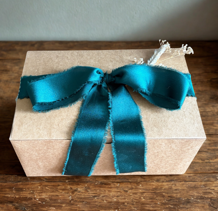 A gift box wrapped in plain paper with a teal satin ribbon tied in a bow on top.