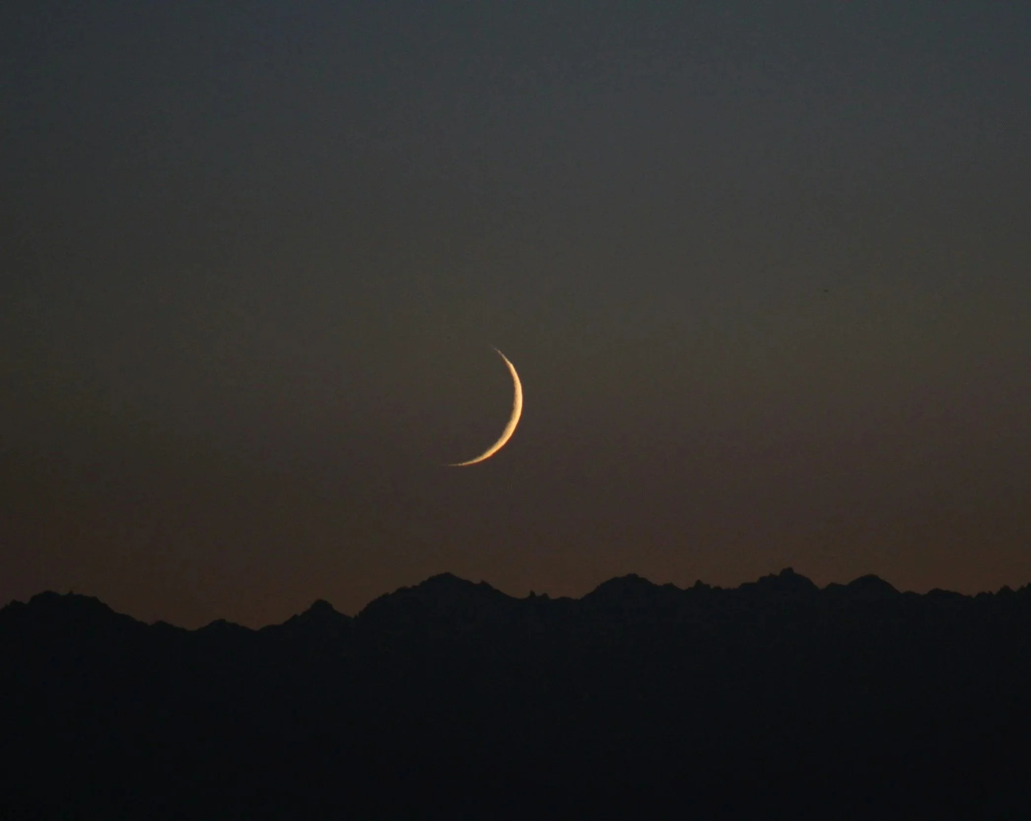 Nighttime sky with a crescent moon and silhouette of mountain range.