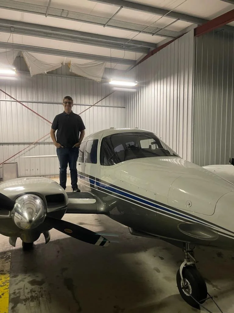 A person standing next to a small private airplane inside a hangar with metal walls and ceiling.