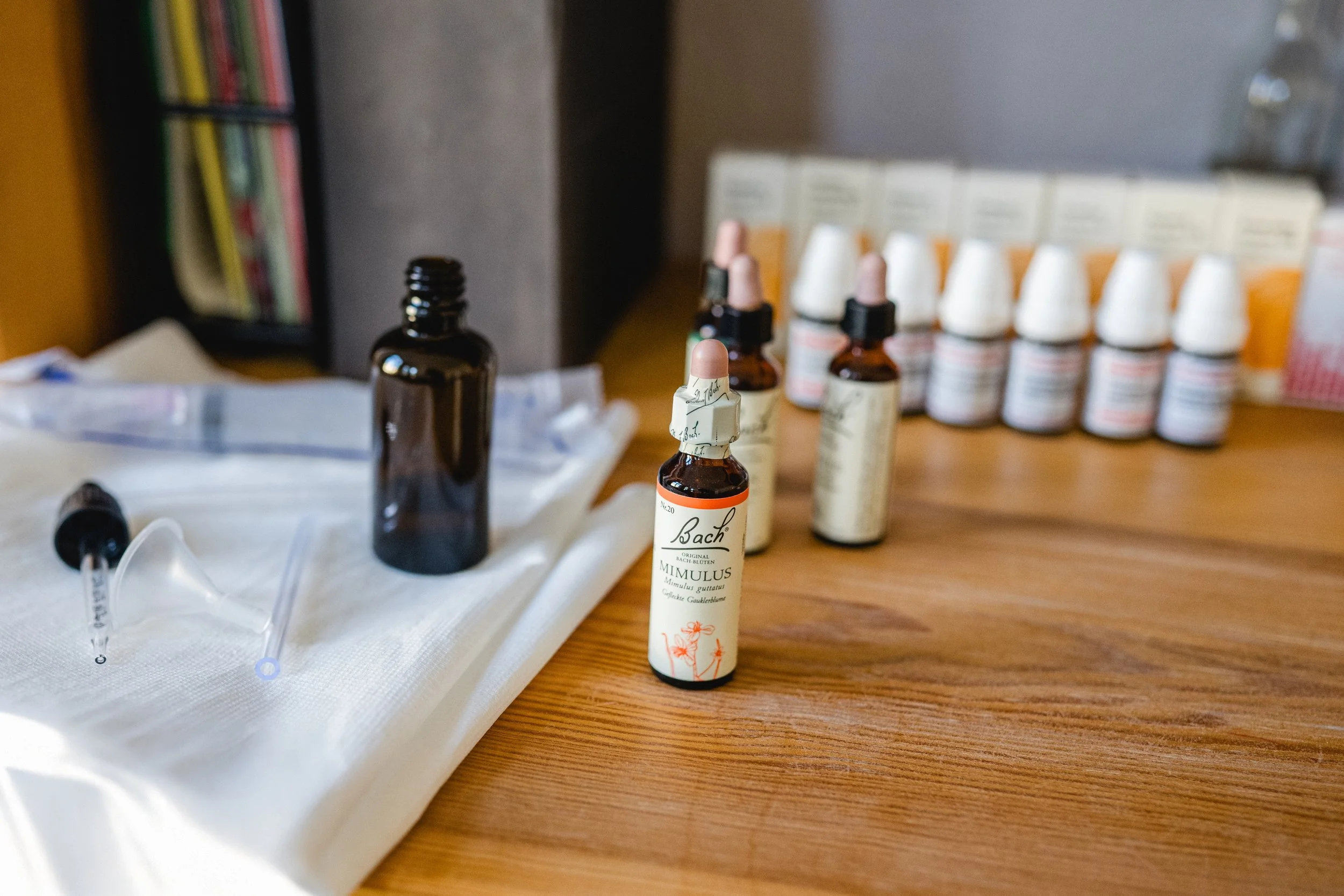 Verschiedene Medikamente und Ampullen auf einem Tisch, darunter eine Flasche mit homöopathischen Globuli und ein Pipettenträger.