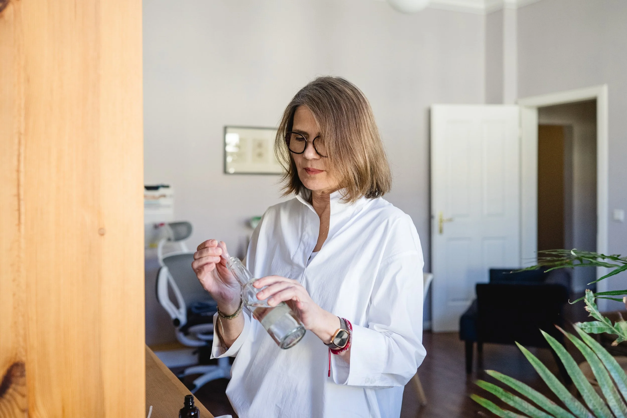 Frau mit Brille in weißem Hemd öffnet eine Flasche im Büro