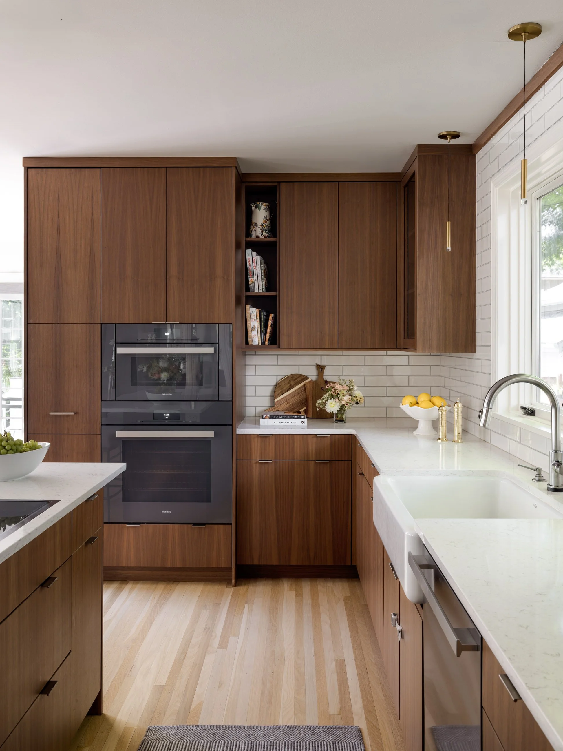 Modern kitchen with wood cabinets, white countertops, a double oven, and a white farmhouse sink next to a window.