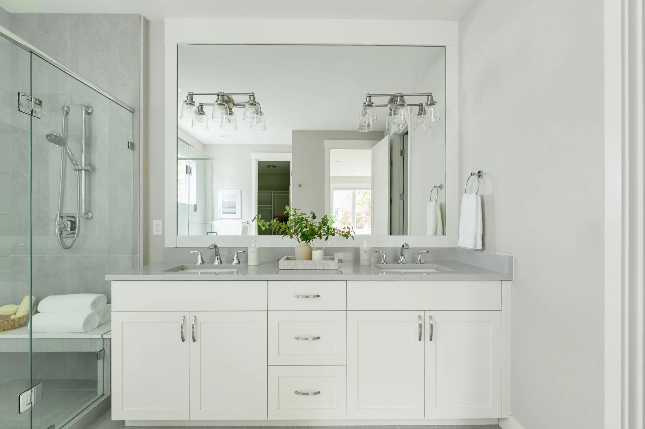 Modern bathroom with a double vanity, large mirror, and a walk-in shower with glass enclosure, minimalist decor, and natural light.