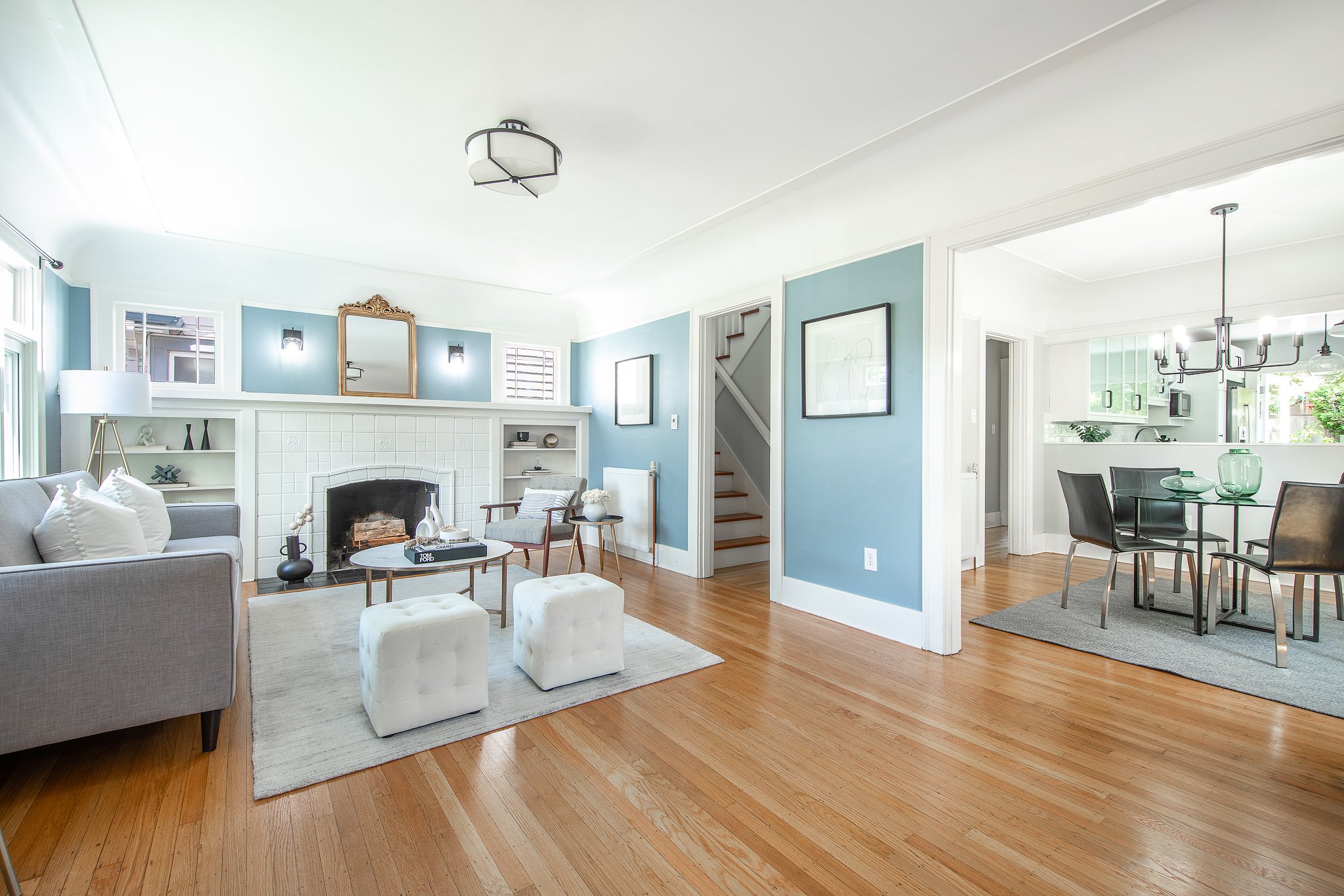 Bright living room with blue walls, white fireplace, gray sofa, white ottomans, wooden flooring, and modern furniture.