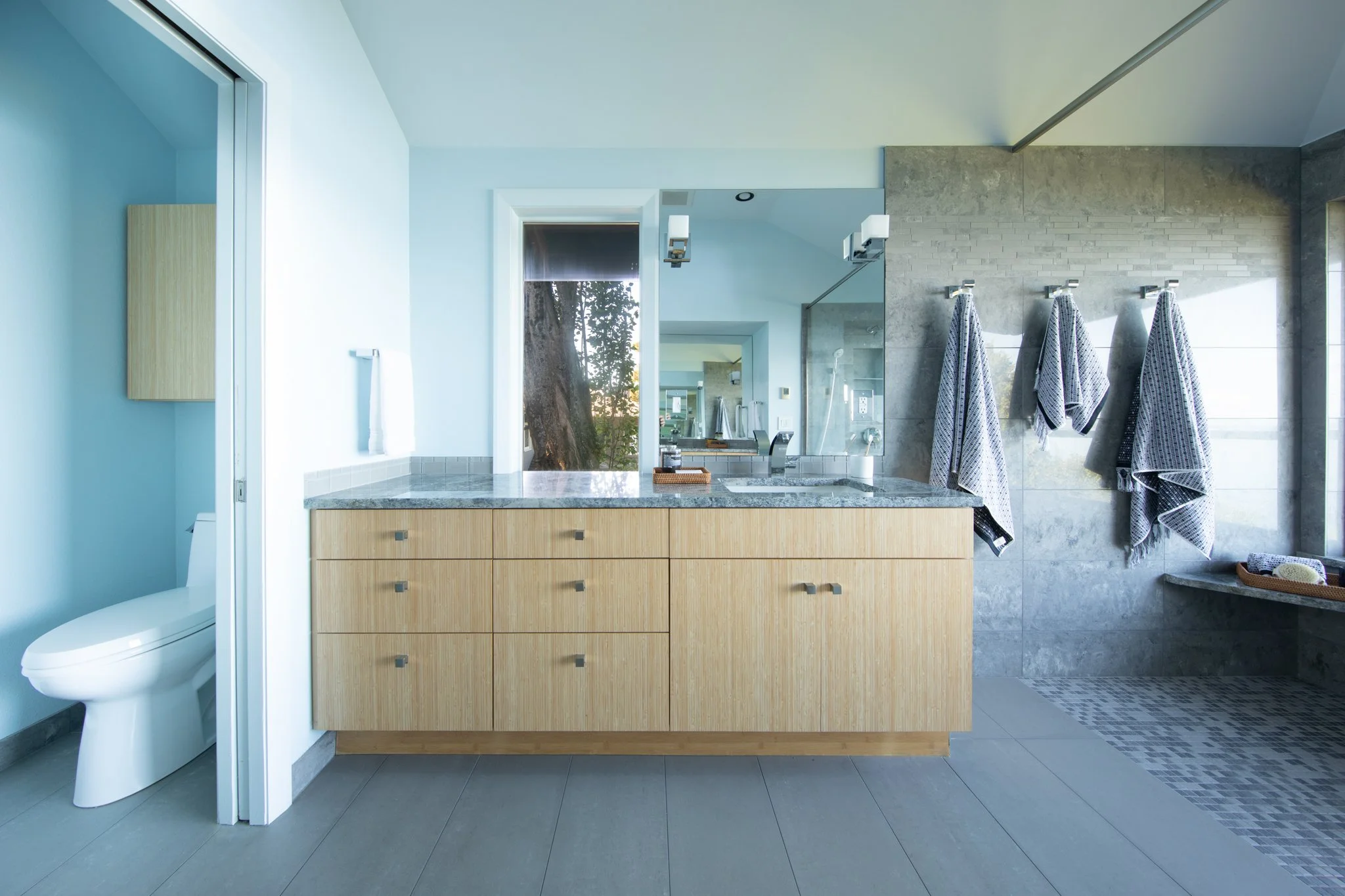 Modern bathroom with wooden vanity, granite countertop, large mirror, and hanging towels on hooks.