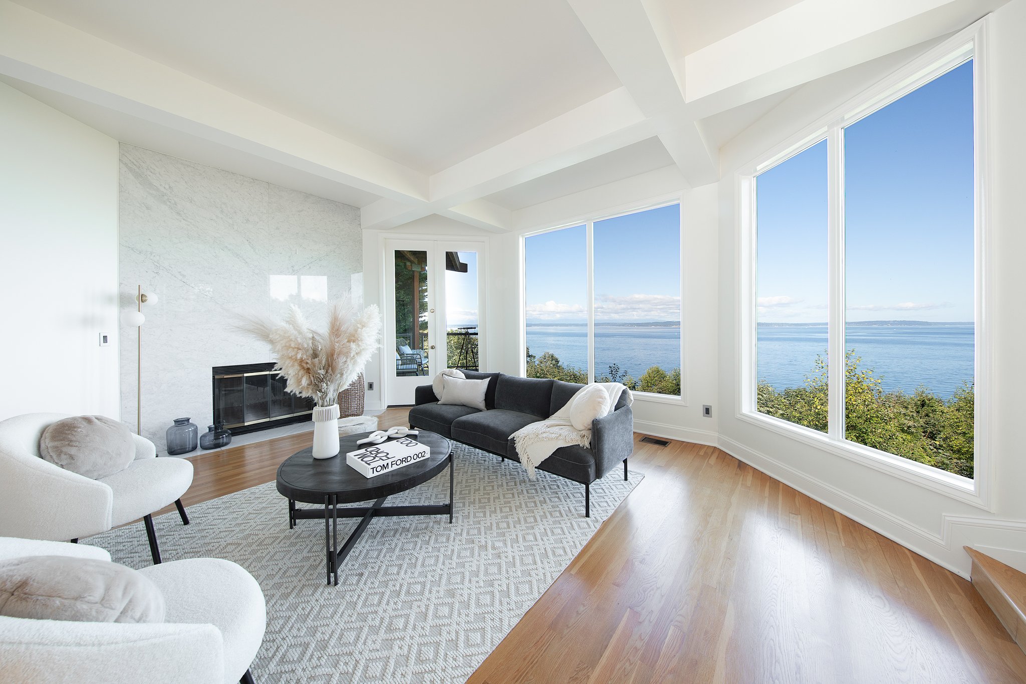 Living room with large windows overlooking water, white walls, modern furniture, and a fireplace.