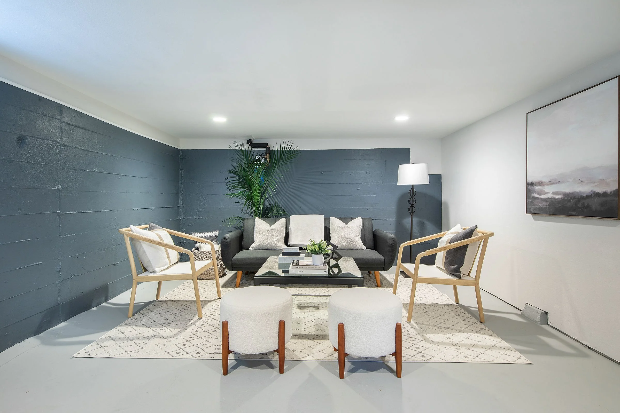 Modern living room with gray brick wall, white ceiling, and minimalist furniture including a black sofa, white armchairs, and a glass coffee table, accented by a large painting and a tall floor lamp.
