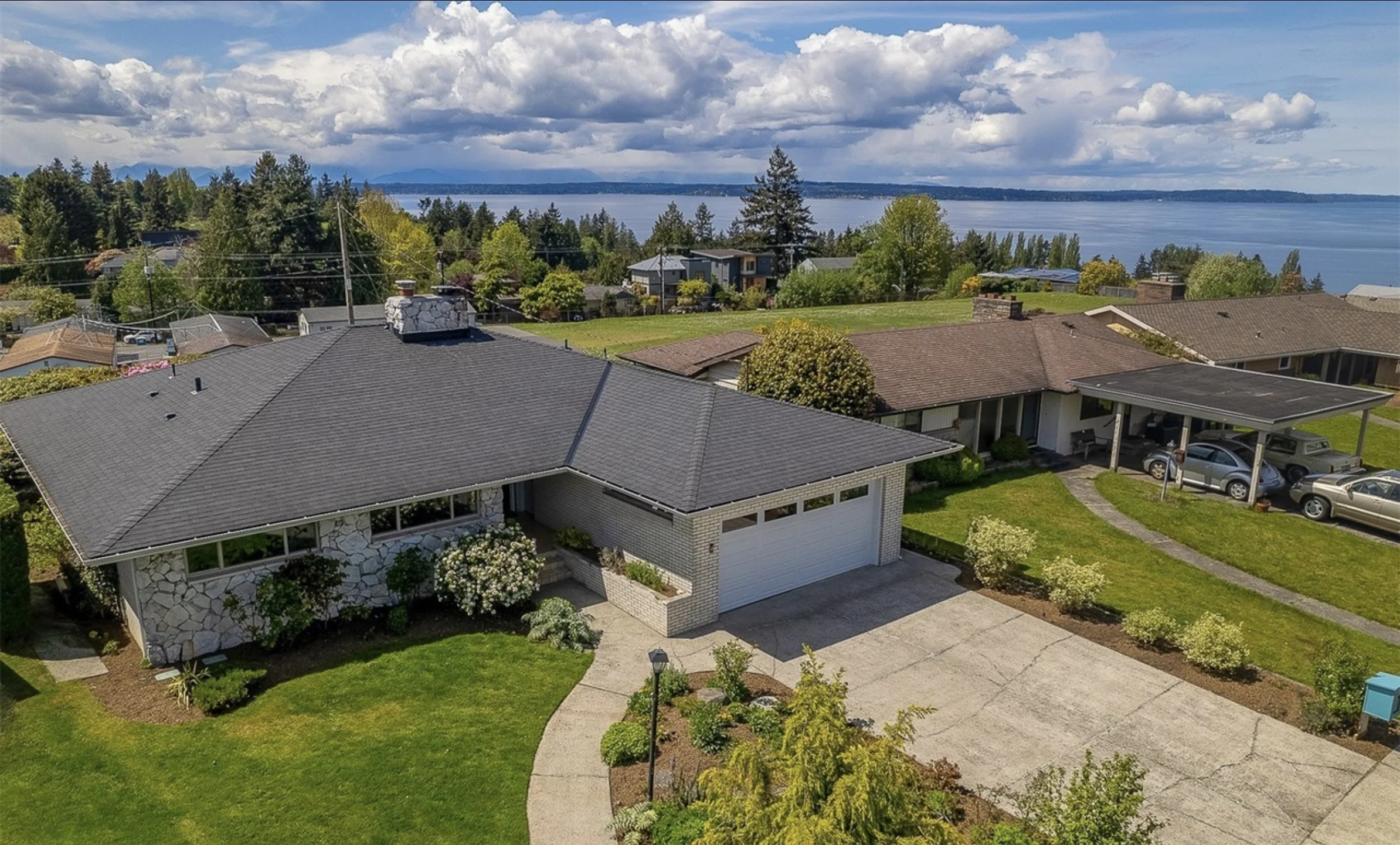 Aerial view of a residential neighborhood near a large body of water with trees, houses, and a cloudy sky.