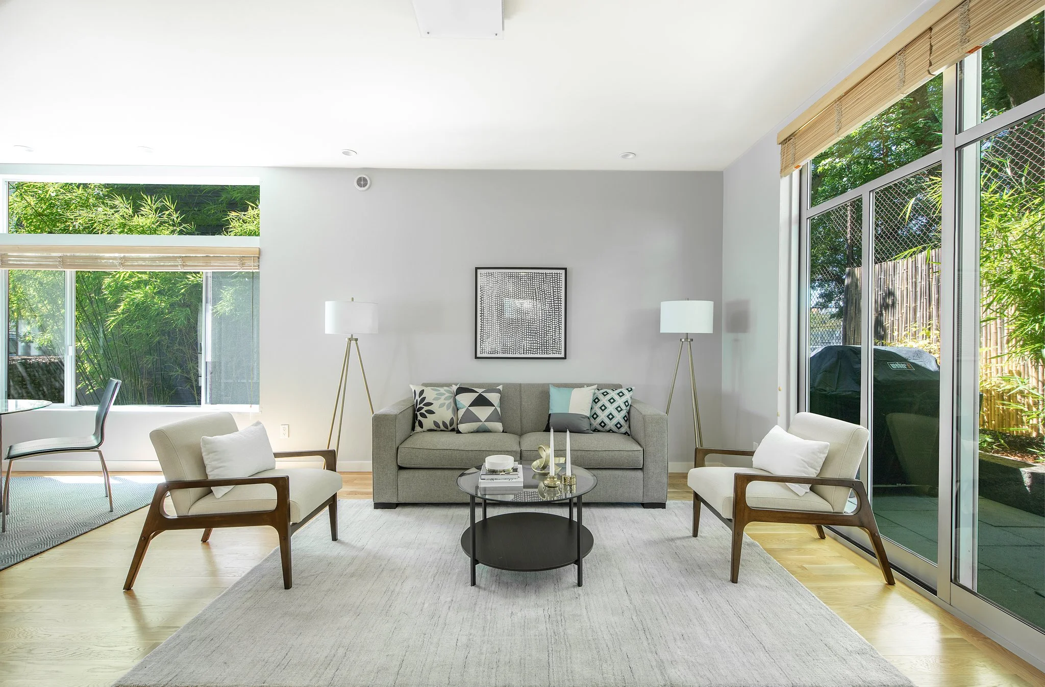 Modern living room with large windows, a gray sofa, armchairs, a round black coffee table, and minimalistic decor.