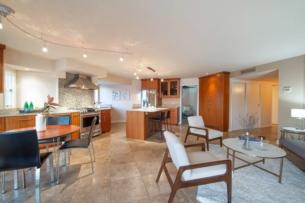 Open-concept living space with kitchen, dining, and seating area, featuring wooden cabinets, modern appliances, and minimalist decor.