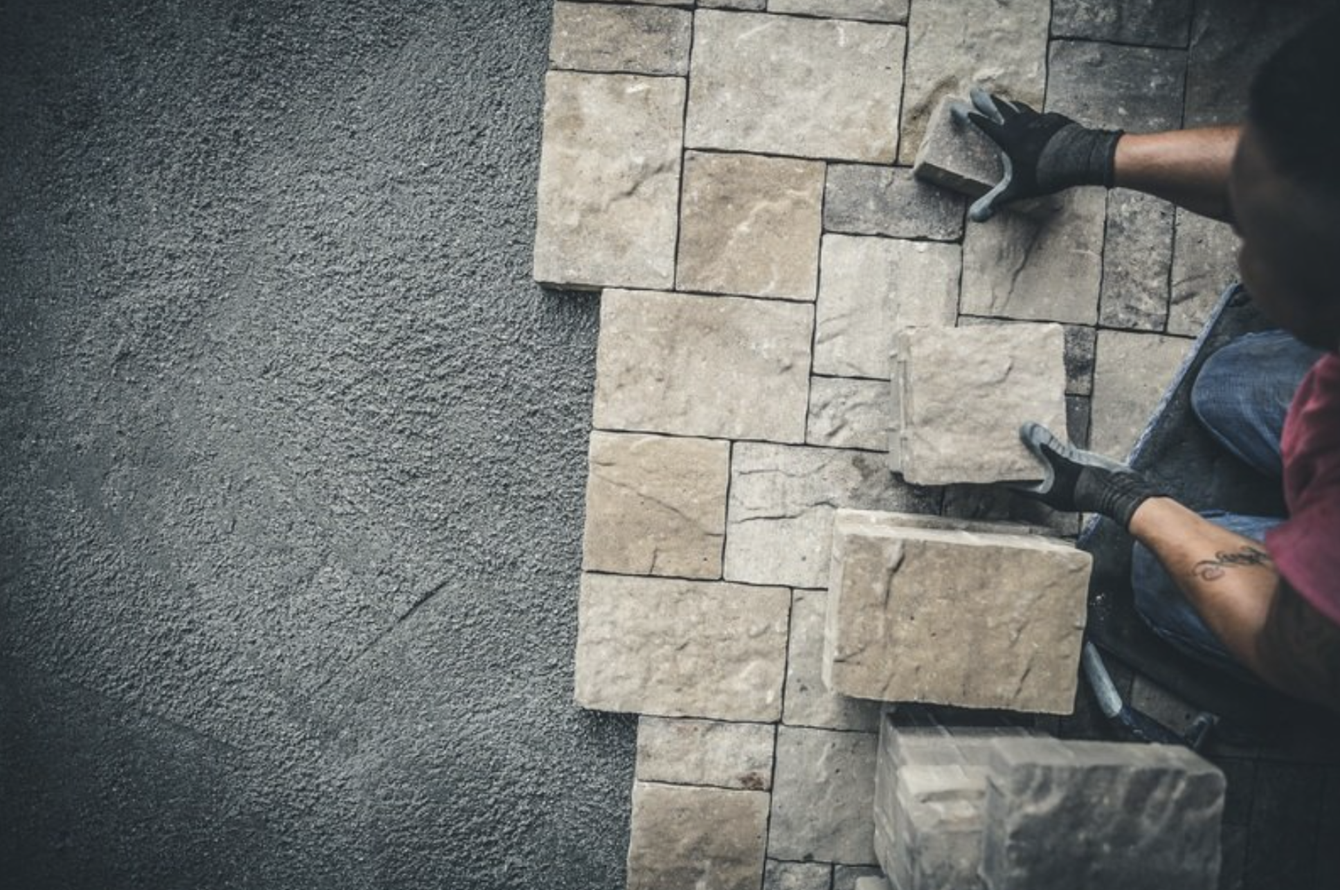 A person laying bricks to construct a wall, with black gloves on their hands, working on the right side of the image.