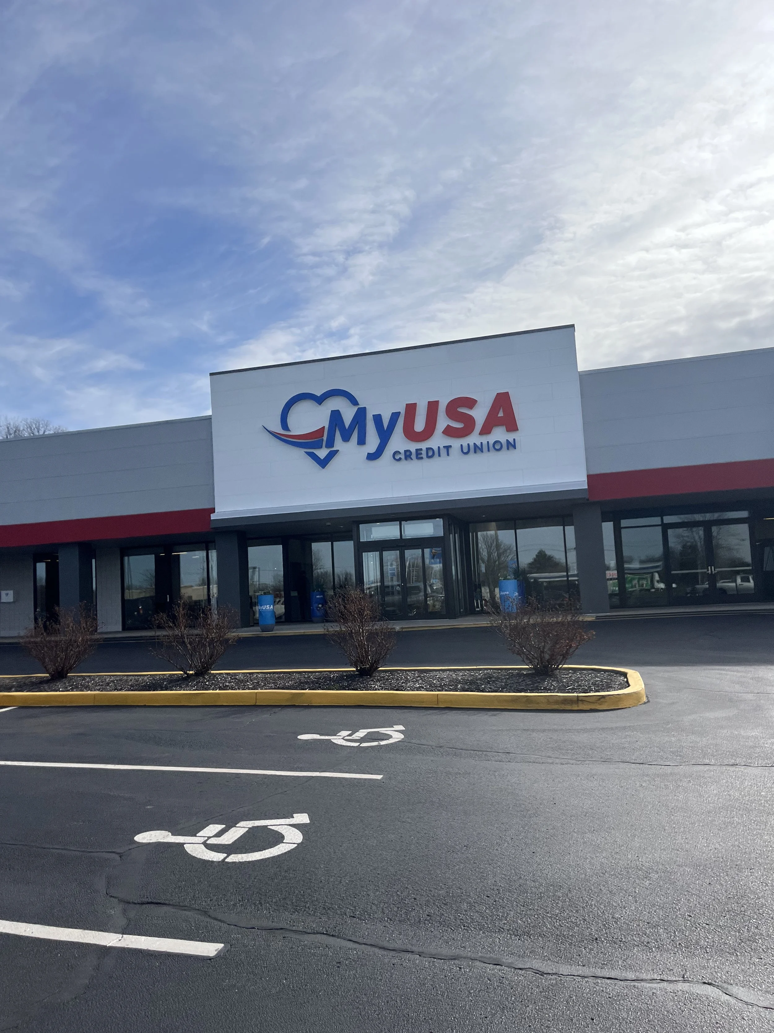 Exterior view of a MyUSA Credit Union building with a parking lot and handicapped parking spaces in the foreground, under a partly cloudy sky.