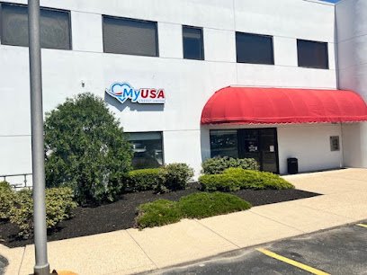 Exterior of a white building with a red awning, bushes, and a sidewalk in front, and a sign that reads 'MyUSA' on the building.