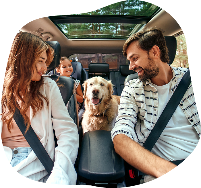 A family of four with a dog in the backseat of a car, smiling and enjoying the trip.