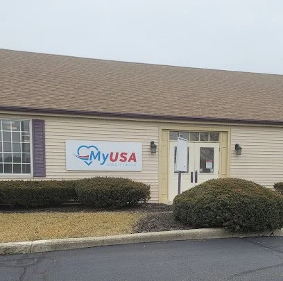 A building with a sign that reads "My USA" outside, with bushes in front and a paved parking area.