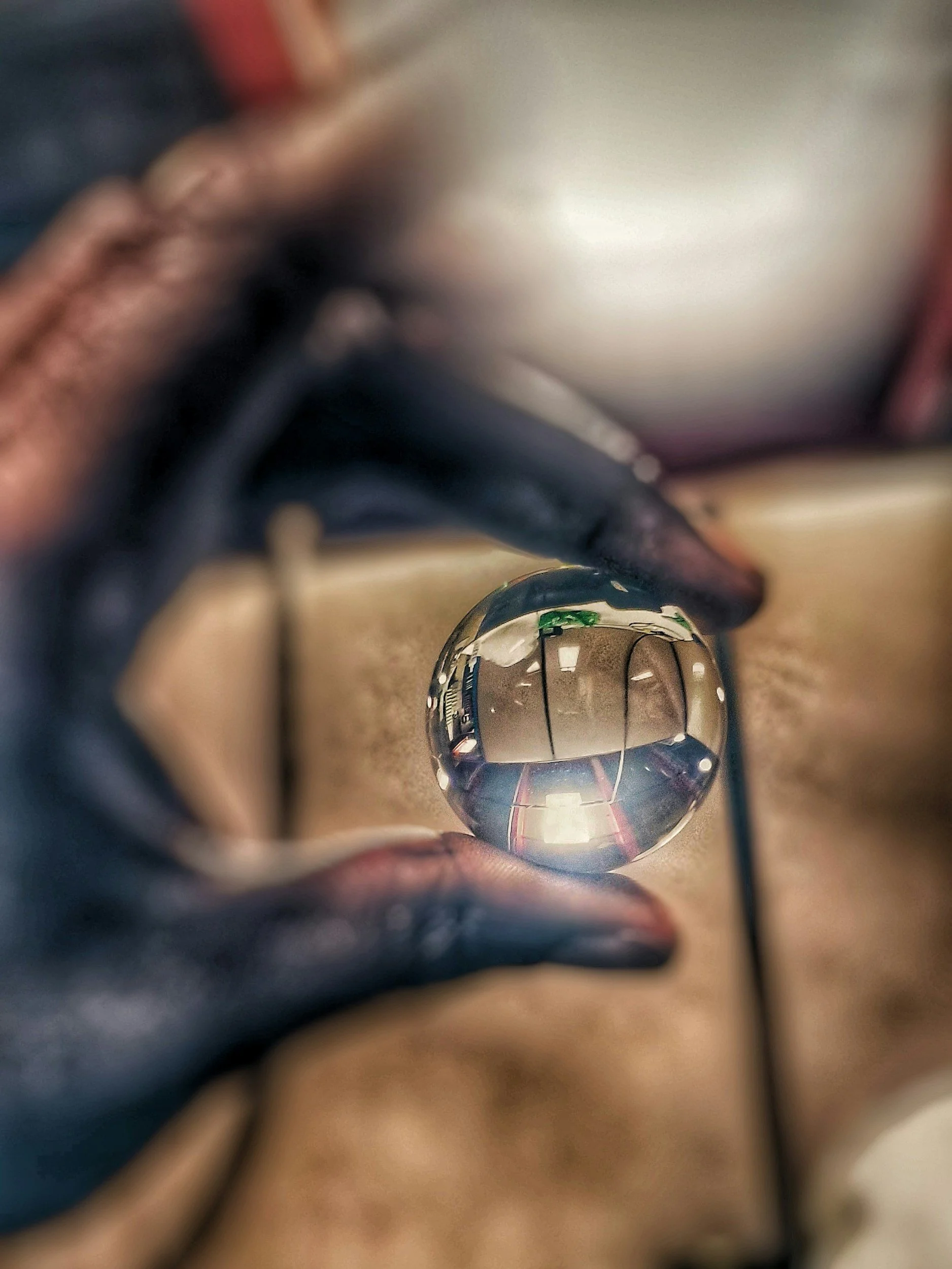 Close-up of a person's hand holding a glass sphere, reflecting the surrounding room including a door and ceiling.