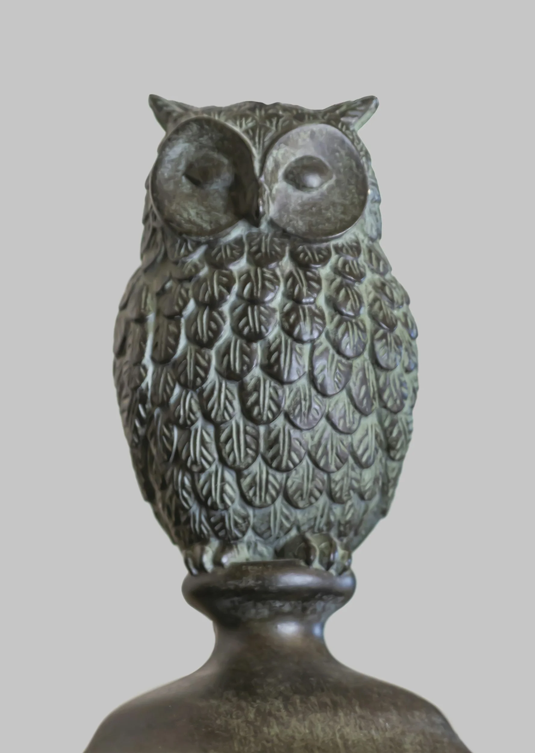 Bronze sculpture of an owl with detailed feather patterns and large round eyes, mounted on a rounded pedestal.