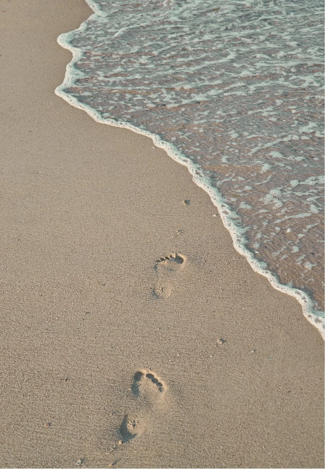 Footprints in the sand on a beach with gentle waves approaching