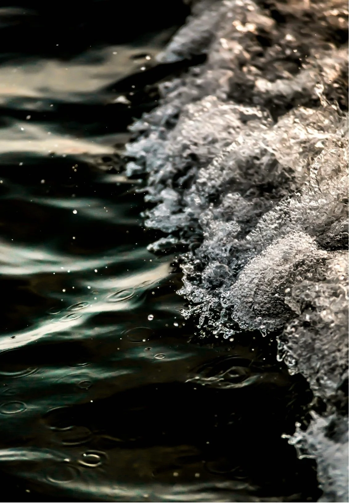 Close-up of water crashing against a rocky shoreline, with bubbles and foam forming at the edge.