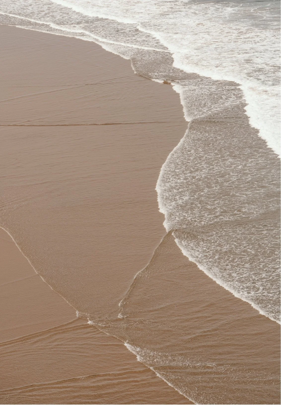 Waves crashing onto sandy beach shoreline with foam and ripples in the water.