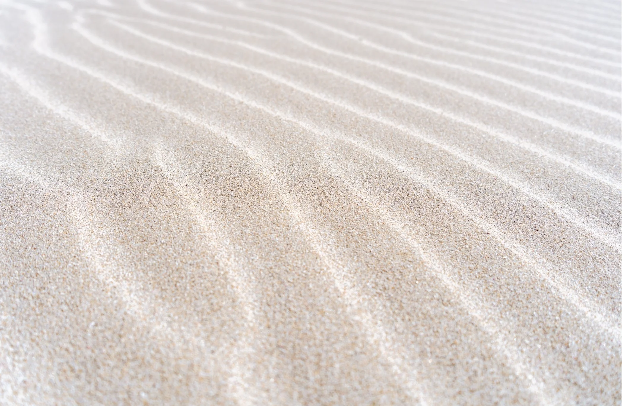 Close-up of textured, light-colored sand with faint, linear patterns