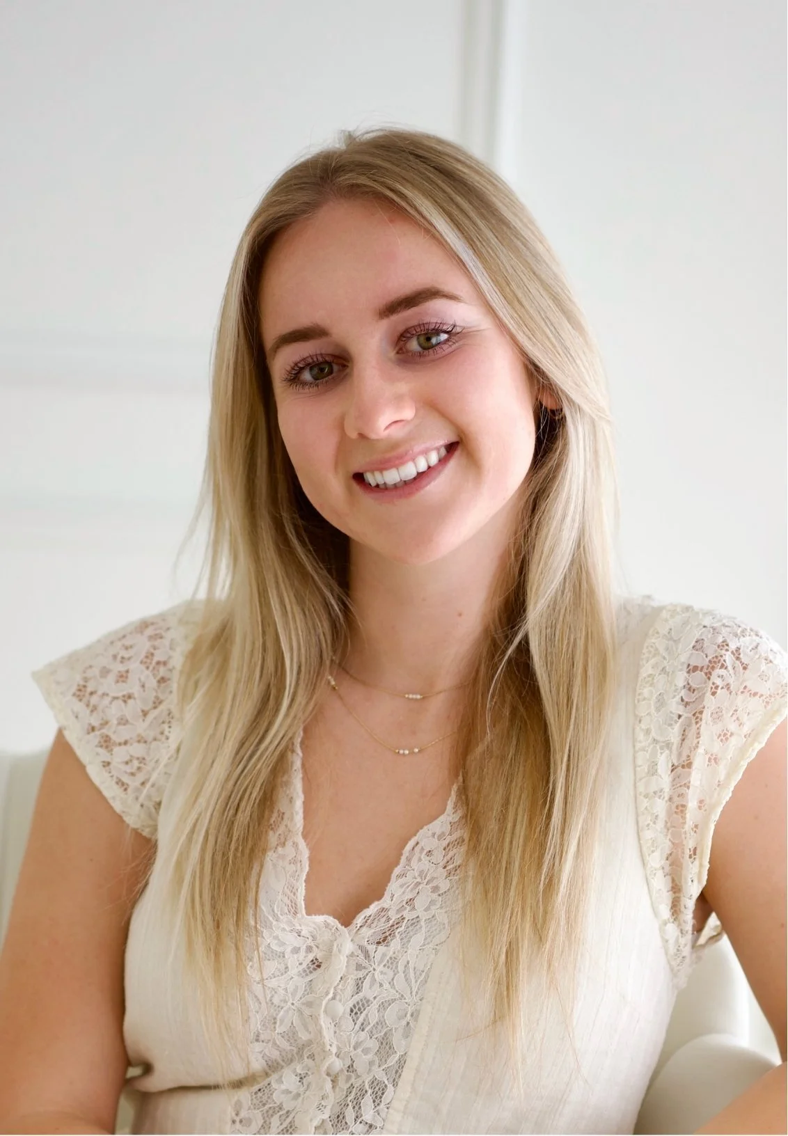 Paige Lewis, administrative coordinator at Soulfire Psychotherapy, with long blonde hair, wearing a white lace top, smiling at the camera, with a light background.