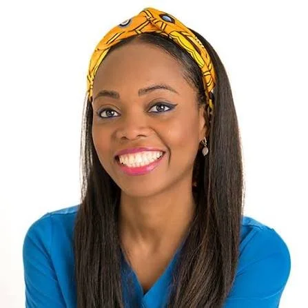 Smiling woman with long dark hair wearing a yellow headscarf and a blue top, portrait against a white background.