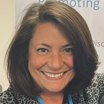 Close-up of a smiling woman with shoulder-length brown hair wearing a patterned top.