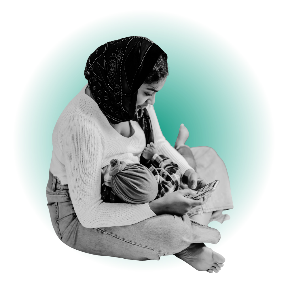 A woman sitting cross-legged, wearing a black hijab and a white sweater, looking at her phone with a child lying across her lap, all within a circular green background.