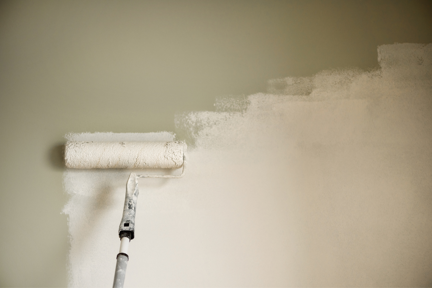 A paint roller applying white paint to a wall.