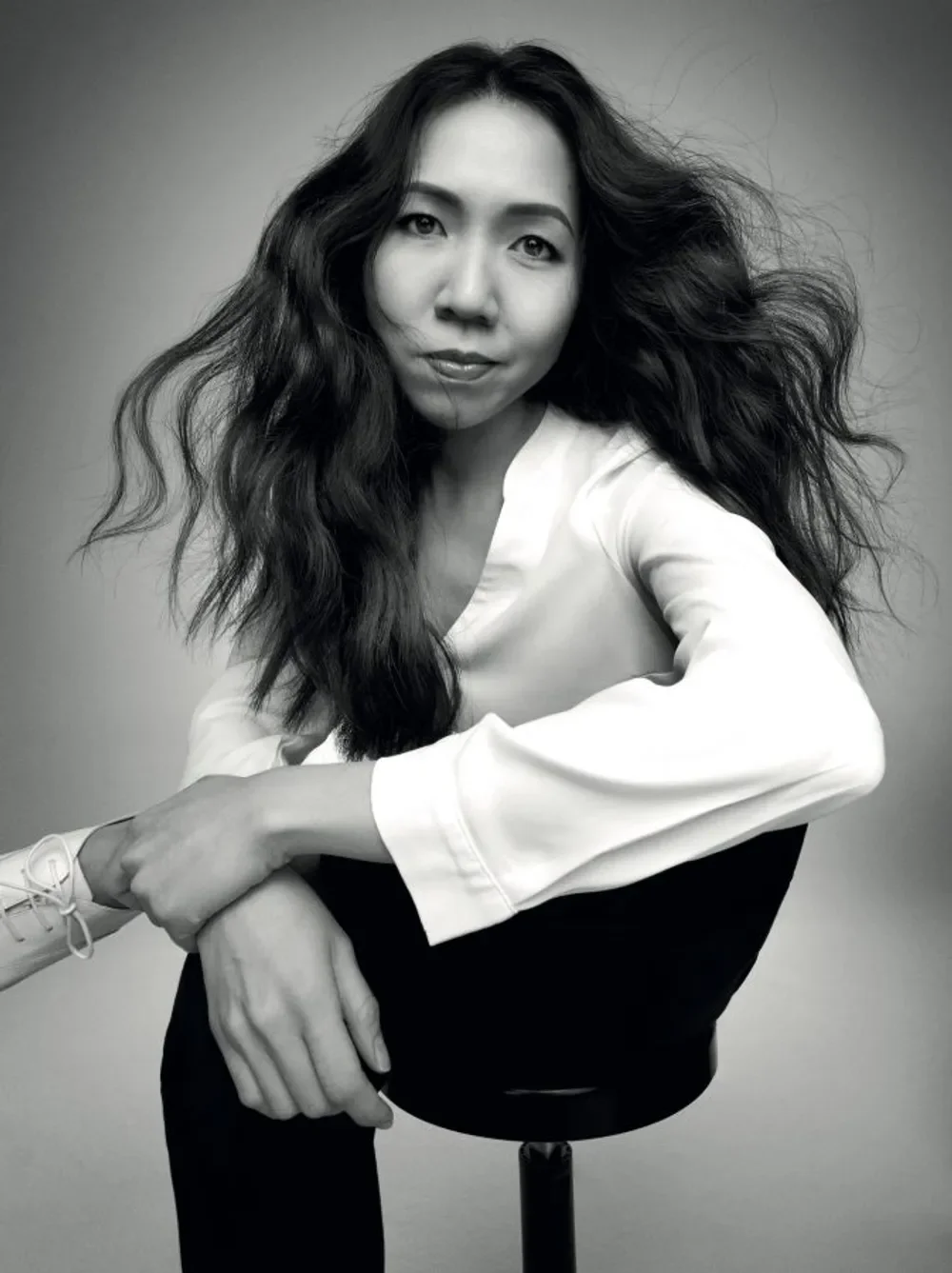 A black and white portrait of Wai-Jia Tam, sitting on a chair, looking at the camera.