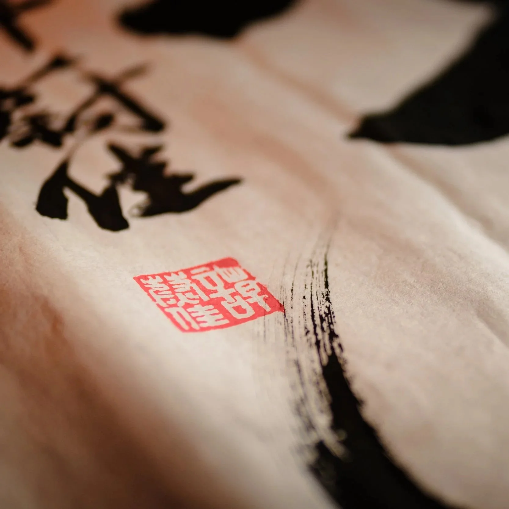 Close-up of Asian calligraphy text on paper with red stamp, ink brush strokes, and traditional style.