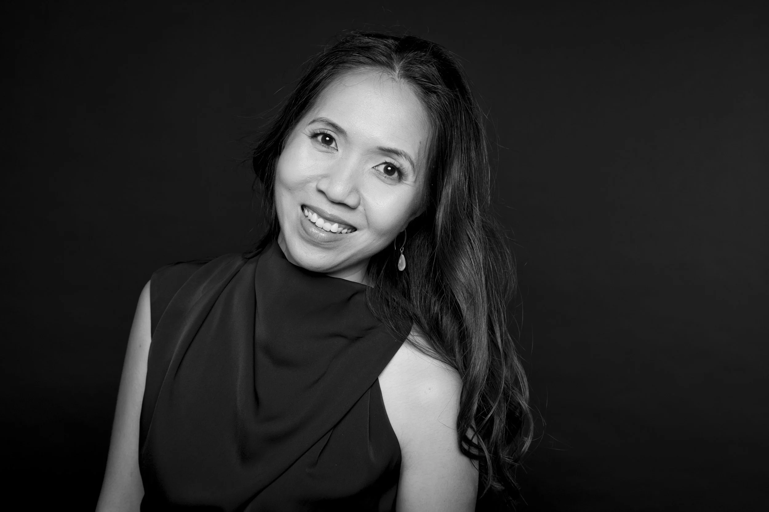 Black and white portrait of Wai-Jia Tam with long wavy hair, smiling, tilting her head to the right.