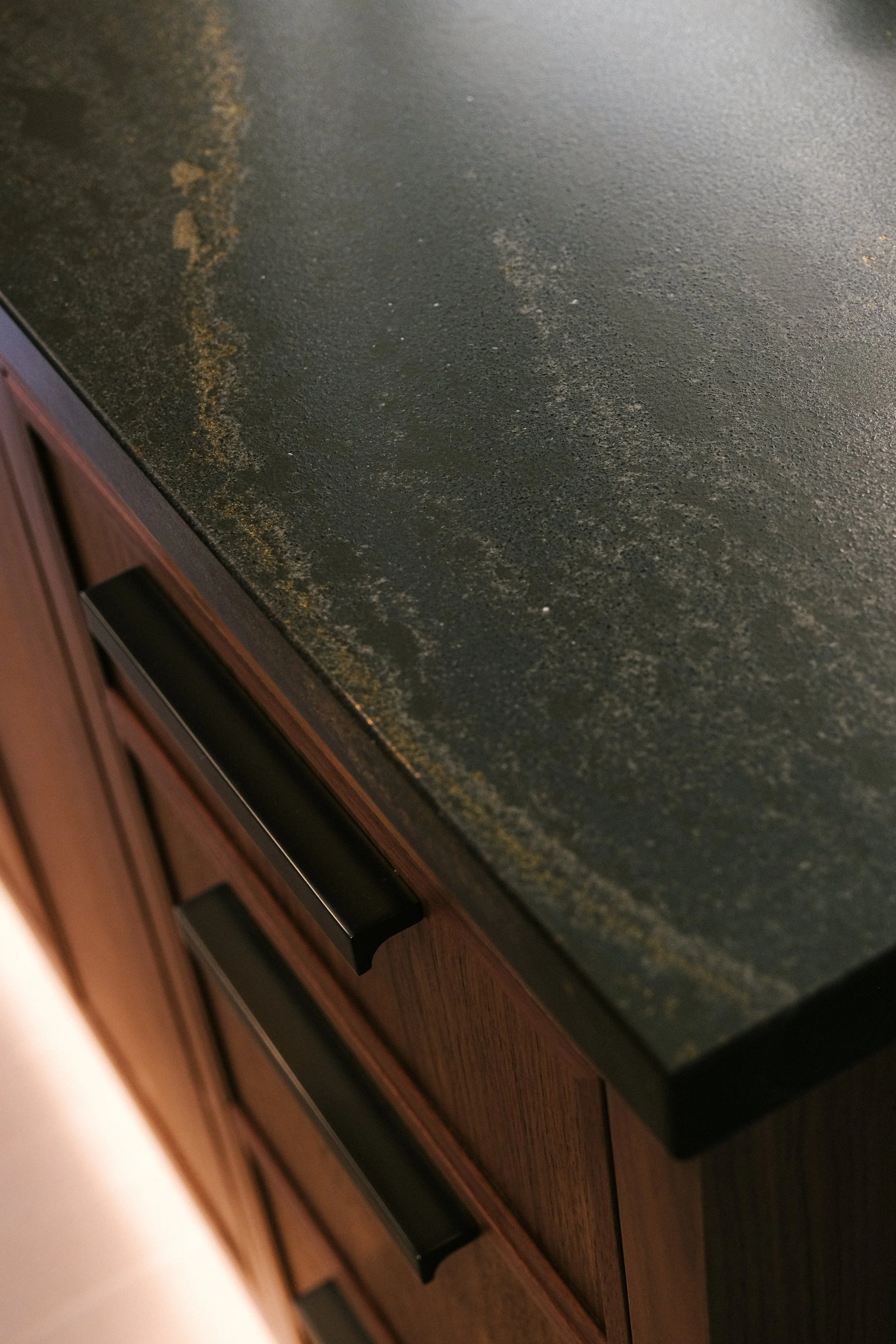 Cambria Remington Brass countertop with subtle brass inlay atop Walnut cabinets featuring matte black metal hardware.
