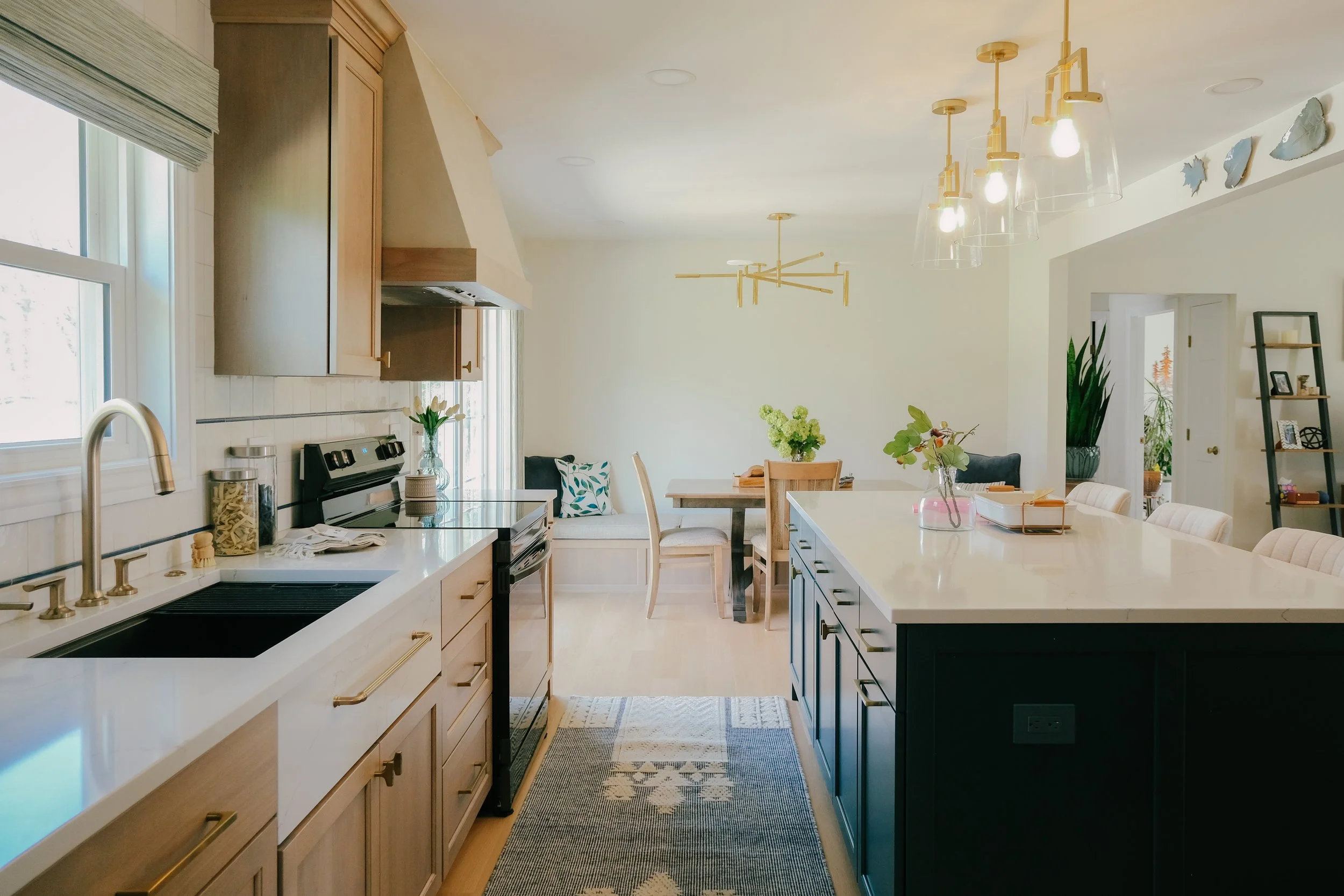 Bright and neutral kitchen with a large island, white quartz countertops, and gold pendant lights. Cozy dining area with an integrated booth.