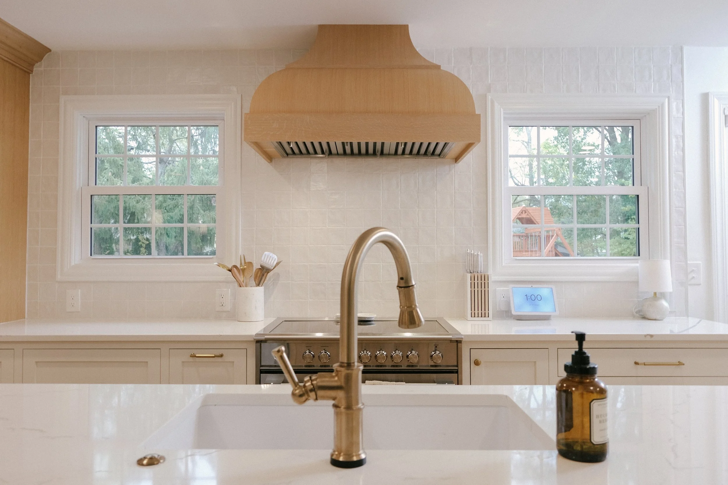 A custom Maple hood overlooks an induction range. White Myorka tile acts as a full-height backsplash behind a Brizo Artesso pull-down faucet.